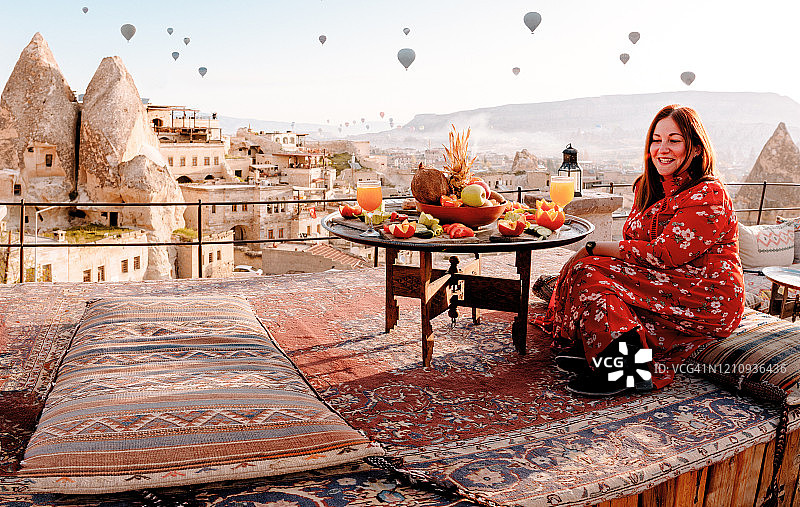 土耳其卡帕多西亚，日出时分，一名身穿红色衣服的妇女站在屋顶上图片素材