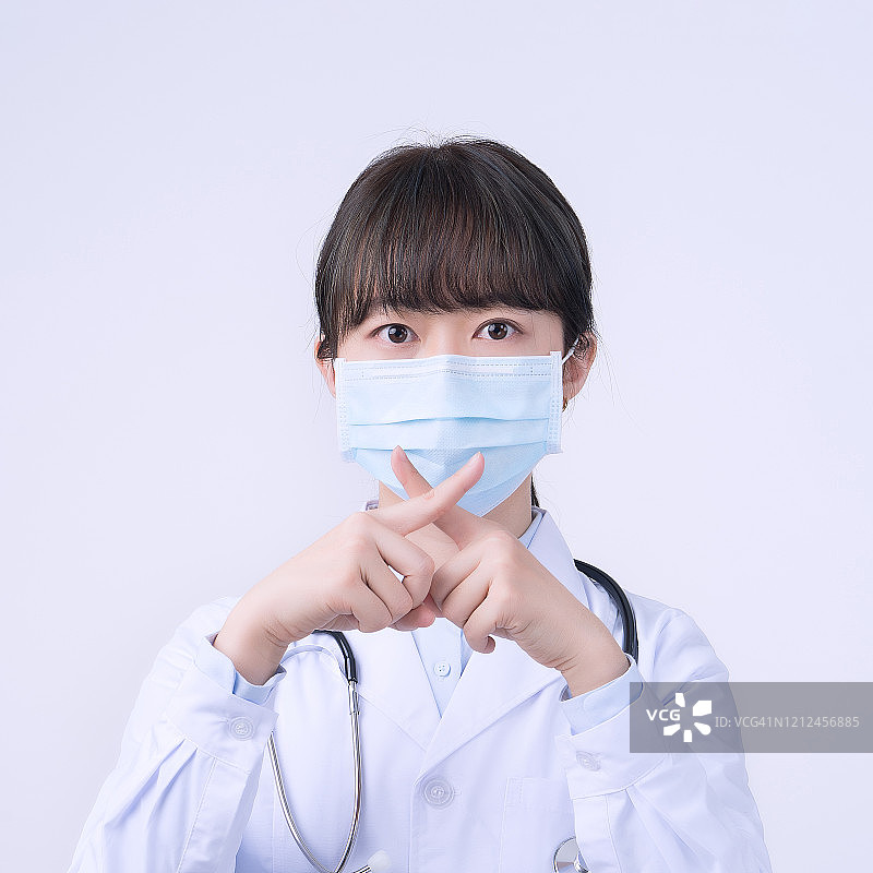 年轻的女医生戴着口罩，做着停止的手势，在白色背景下表示没有隔离，拒绝病毒疾病。图片素材