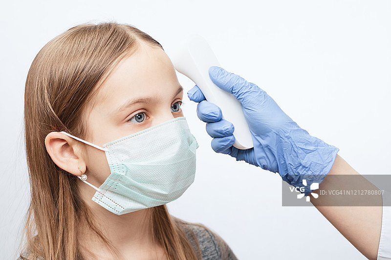 医生用红外体温计检测戴口罩的女孩体温——流行病毒爆发概念图片素材