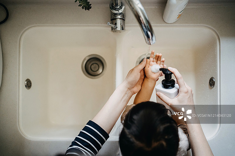 头顶的视图，一个母亲用肥皂给小女儿的手和洗他们的手一起在水槽图片素材