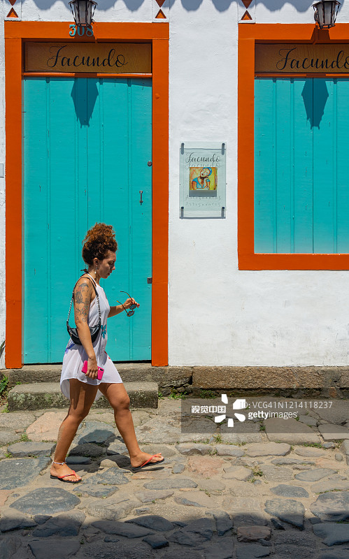 在巴西历史名城帕拉蒂，一名身份不明的女子走过彩色殖民建筑前的鹅卵石街道。图片素材