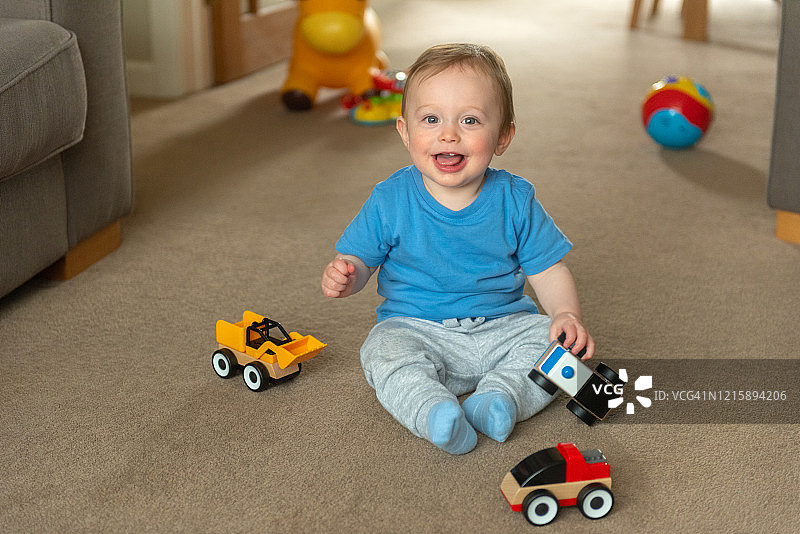 10个月大的小男孩坐在地板上玩玩具车图片素材