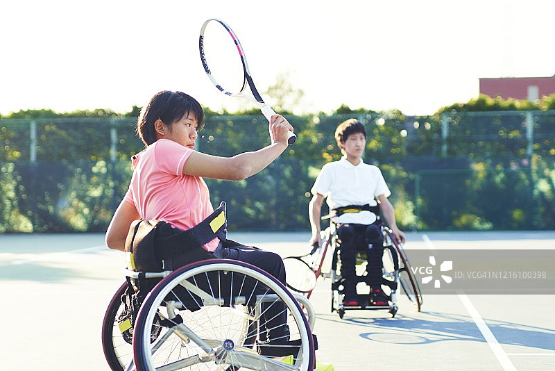 十几岁的女孩和十几岁的男孩都坐在轮椅上在网球场打网球图片素材