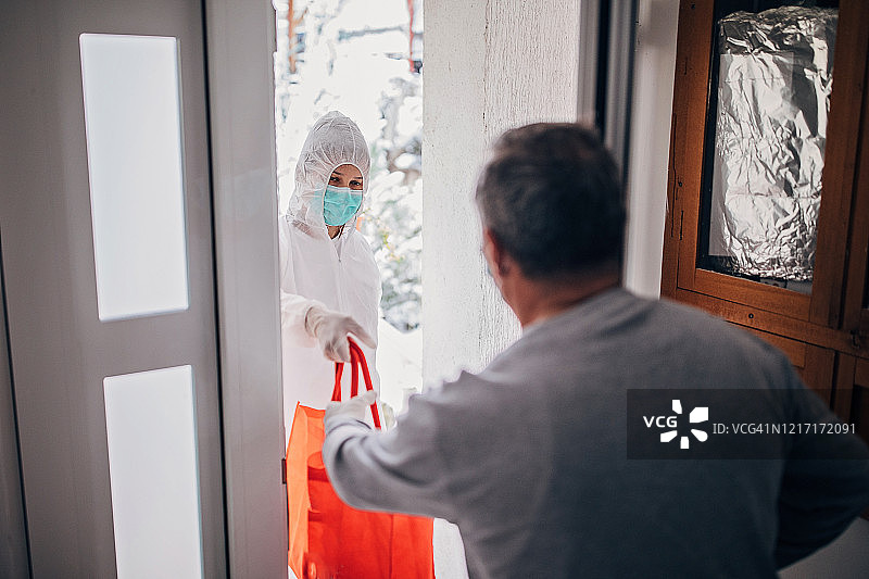 世界卫生组织的志愿者将食品杂货送到门口的一位老人面前图片素材