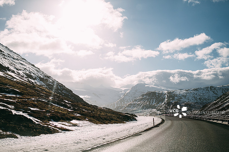 在阳光明媚的冬日，冰岛雪山之间的空旷道路图片素材
