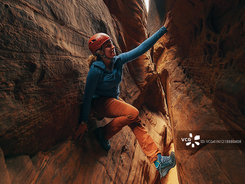 一个年轻的女人爬过狭缝峡谷图片素材
