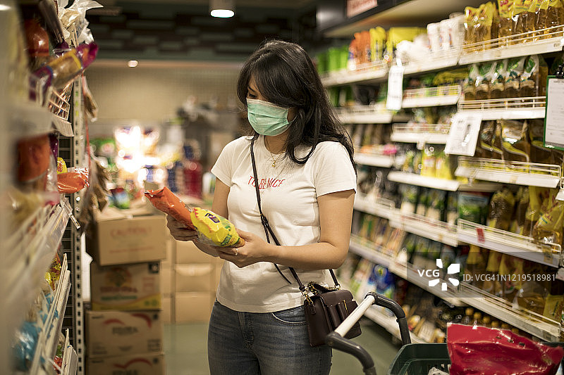 年轻女子在杂货店购物，戴着防护医用口罩图片素材