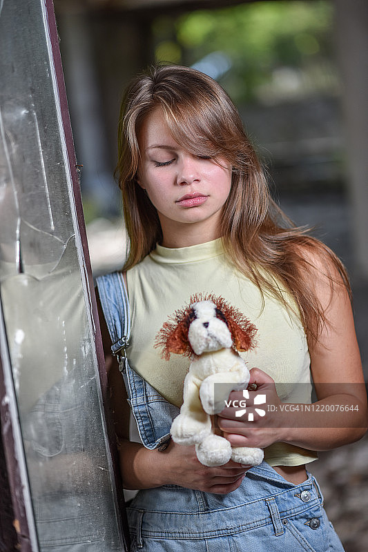 一个悲伤孤独的女孩在废弃的建筑里拿着小狗玩具图片素材