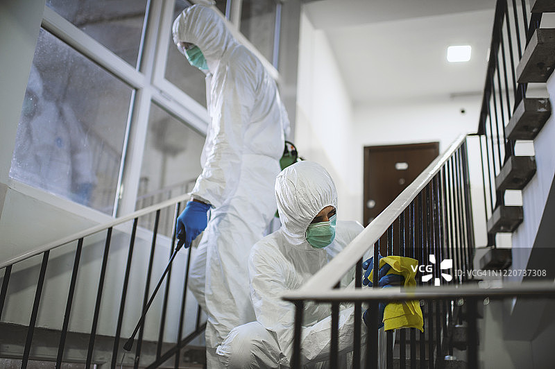 身穿白色化学防护服的男子正在为建筑物的走廊和台阶消毒。图片素材