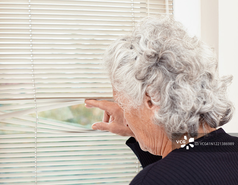 一位老妇人独自站在那里，忧伤地望着窗外图片素材