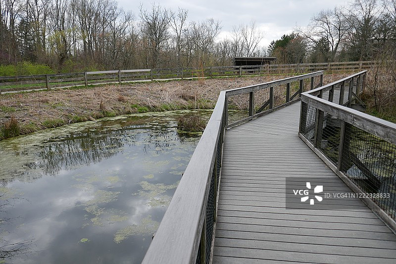 木桥跨越池塘，在公园里有忧郁的天空倒影图片素材