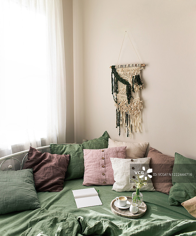 卧室内部有亮绿色的亚麻布，床上有粉色的靠垫和棉质流苏。
从上面的自然有机亚麻床单和枕头在舒适简单的卧室，书，咖啡和简单的花在大理石托盘上。早上的概念。图片素材