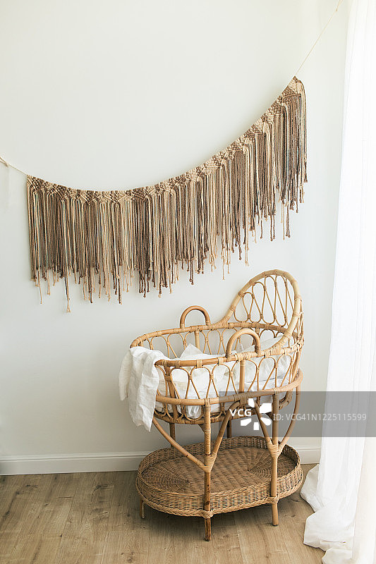 时尚的斯堪的纳维亚新生儿托儿所与天然藤摇篮。现代室内，白色背景墙，木制家具和棉花手工棕色流苏墙上。图片素材
