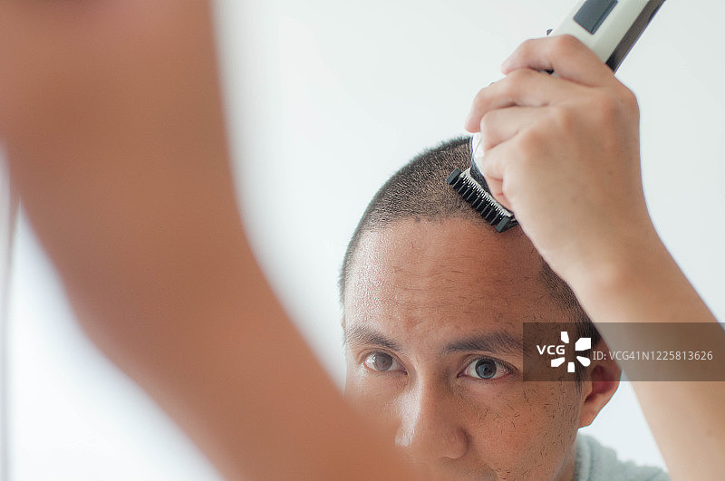 一名年轻的东南亚男子在家里用无线电剪自己的头发图片素材