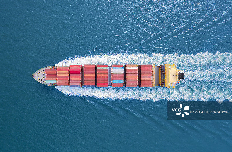 航拍俯视图集装箱货轮以美丽的波浪图案全速行驶在海上，用于商业物流、进出口、航运或运输。图片素材