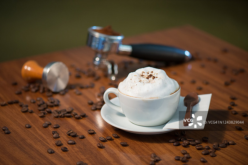 木桌上白杯子里的卡布奇诺咖啡和咖啡豆图片素材