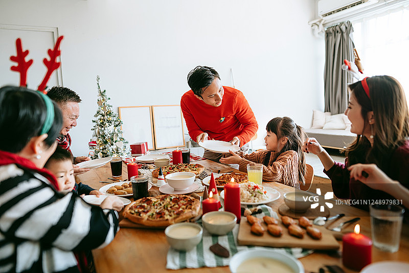 快乐的亚洲多代家庭一起庆祝圣诞节，在圣诞节聚会期间在家里传递和分享食物图片素材