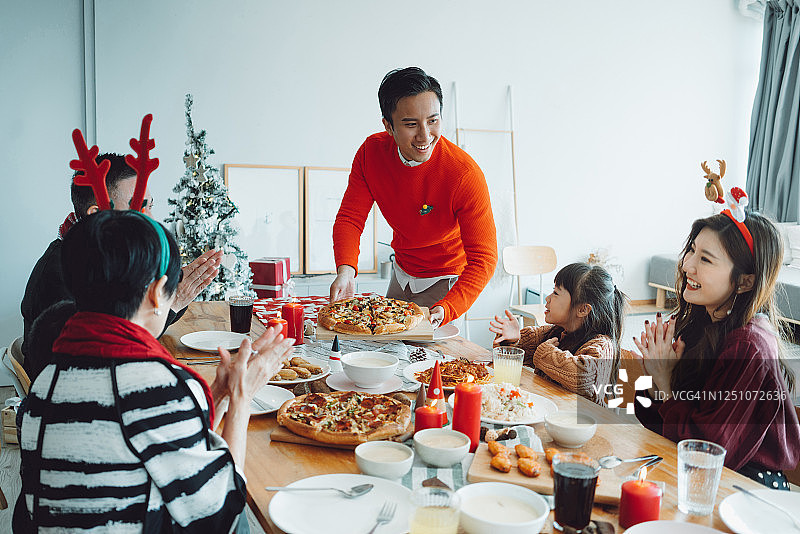 快乐的亚洲多代家庭一起庆祝圣诞节，微笑的年轻人在圣诞派对期间在家为家人提供食物图片素材