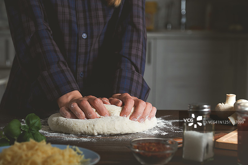 在家里的木桌上用蔬菜和蘑菇烹饪意大利素食披萨。女人用手揉面，揉面。一步一步的指导，自己做。步骤1。图片素材