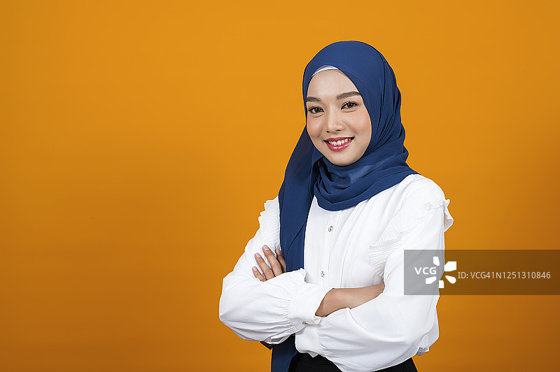 工作室拍摄了一名兴高采烈的穆斯林女子，她双臂交叉站在那里，背景是橙色的。图片素材