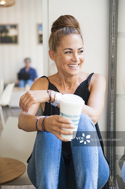 一幅笑着的女人抱着小面包坐在咖啡店里望着窗外的肖像图片素材
