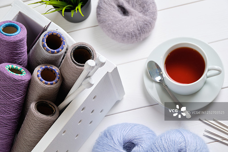 彩色的意大利毛线、毛线和毛线球，编织针，在一个木箱里，在白色的背景上。编织的概念，针线活。旁边是一盆花和一杯茶。图片素材