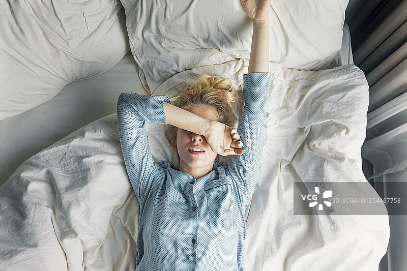 周末早晨:一个美丽的金发女人穿着蓝色睡衣躺在床上图片素材