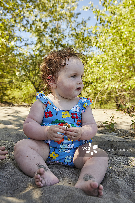 一个婴儿坐在沙滩上，看着镜头外的人。图片素材
