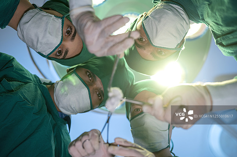 医院手术团队的低角度视图。外科主任拿着纱布清洗伤口。他们穿着绿色的手术服。专业职业，医疗保健。图片素材