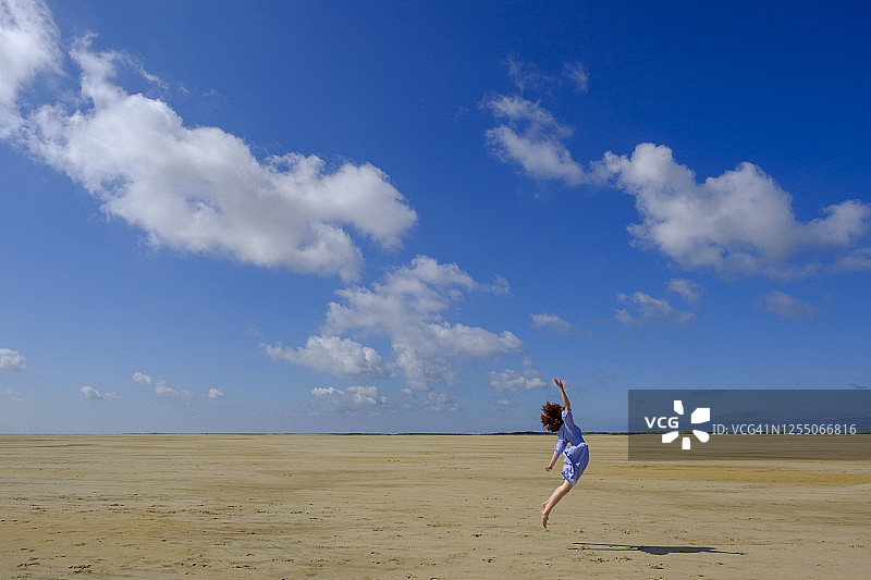 在阳光明媚的日子里，一个少女在海滩上蹦蹦跳跳图片素材