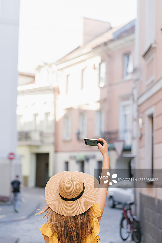 女人在城市巷子里用智能手机自拍的后视图图片素材