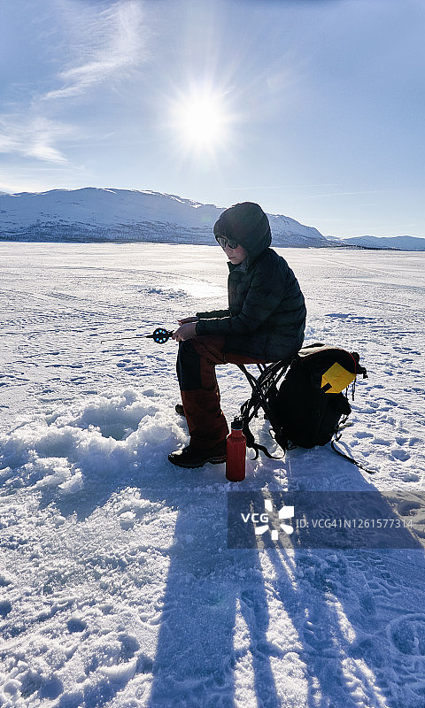在瑞典Vasterbottens Lan的冰湖上，男孩在冰上钓鱼。图片素材