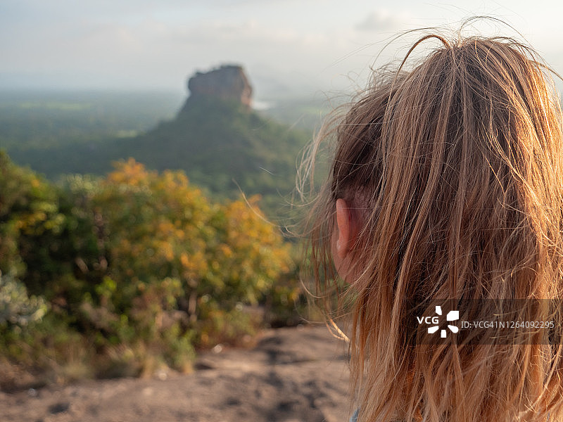 年轻女子站在岩石上日落凝视美丽的丛林自然景观的后视图图片素材