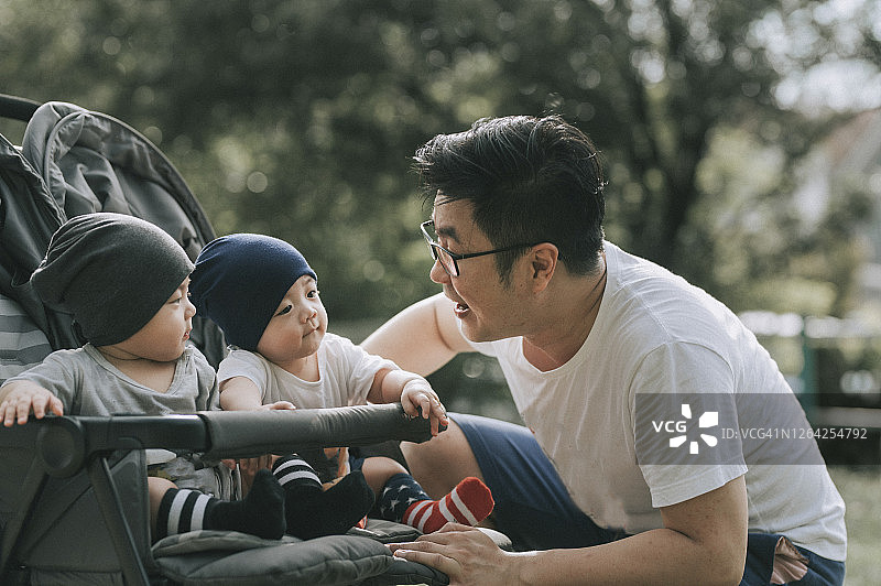 一个年轻的亚洲华人家庭在周末和他们的双胞胎儿子一起在公园玩图片素材
