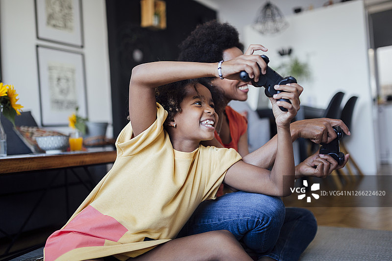 一个快乐的非裔美国家庭的侧面图，母亲和女儿在家里玩电子游戏图片素材