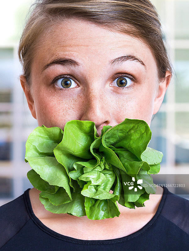 一个嘴里塞着生菜的女人，健康饮食图片素材