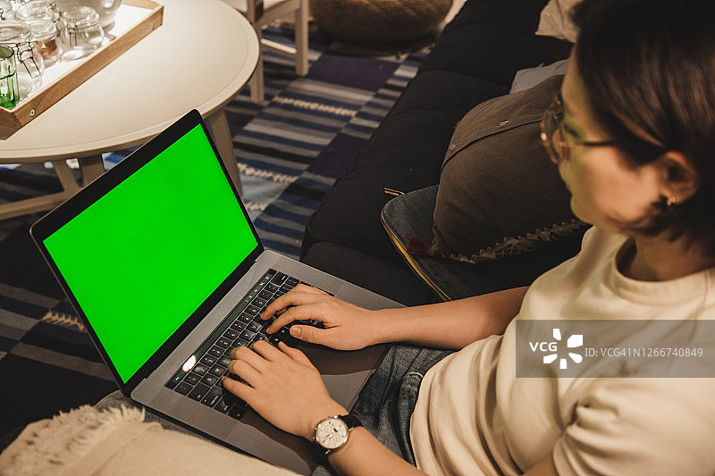 一个亚洲女人坐在沙发上用一台彩色键笔记本电脑图片素材