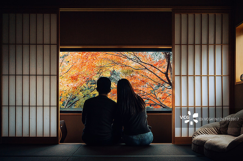在一间传统日式公寓里，一对相爱的亚洲年轻夫妇肩并肩地坐在窗前，一边聊天一边欣赏着白天美丽的自然风光图片素材