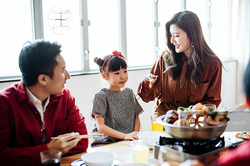 三代快乐的亚洲家庭庆祝春节，享用美味的传统中国菜团圆饭，母亲给女儿端菜图片素材