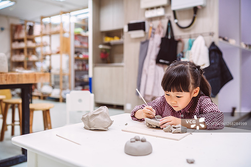 可爱的小女孩在陶瓷作坊用陶土和工具手工制作陶器图片素材