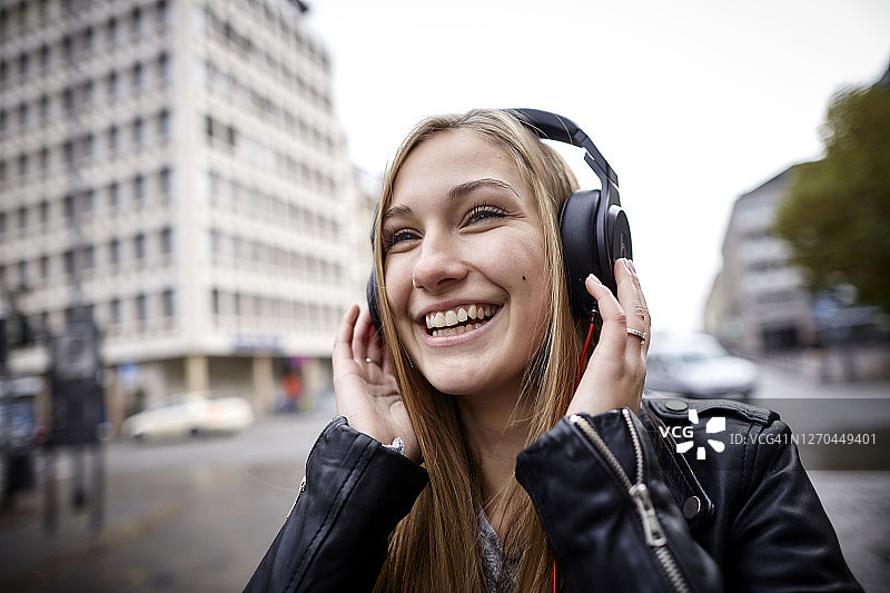 快乐的年轻女子戴着耳机在城市里图片素材