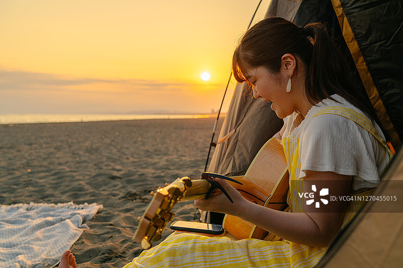 年轻的女吉他手在海滩上弹奏吉他和激情歌唱在日落的夏天图片素材
