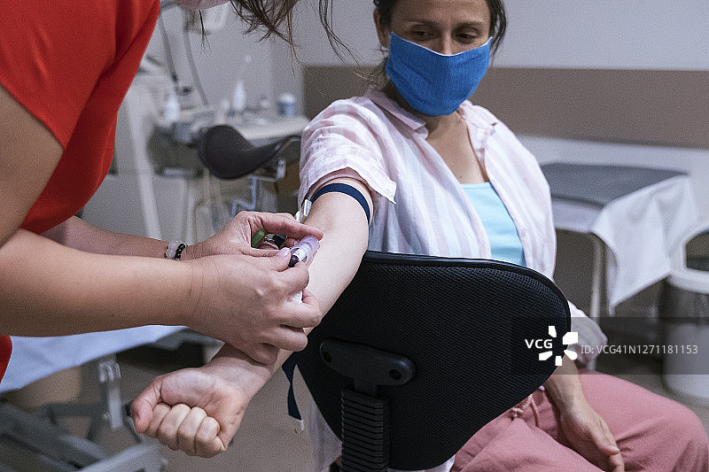2019冠状病毒病大流行期间献血。一名年轻女子戴着防护面罩在献血。图片素材