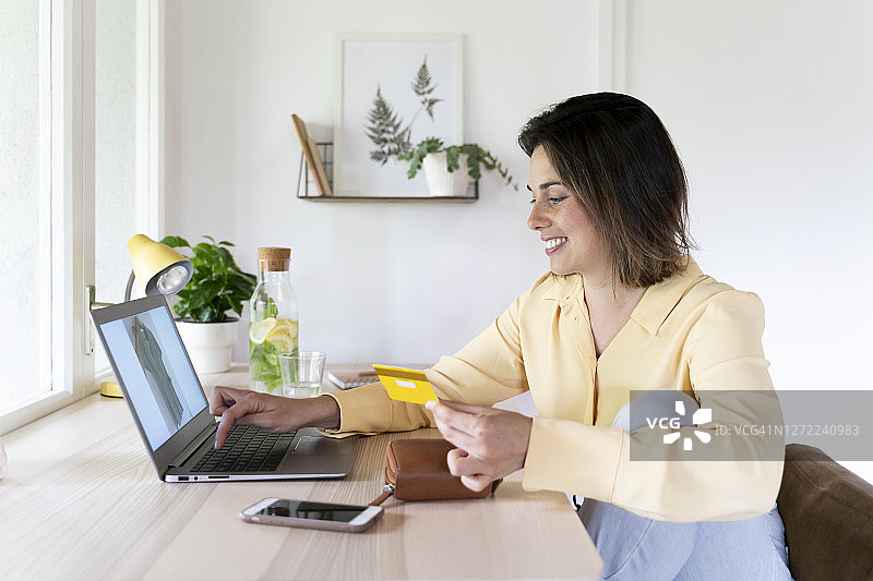 快乐美丽的年轻女子使用笔记本电脑在家里网上购物图片素材