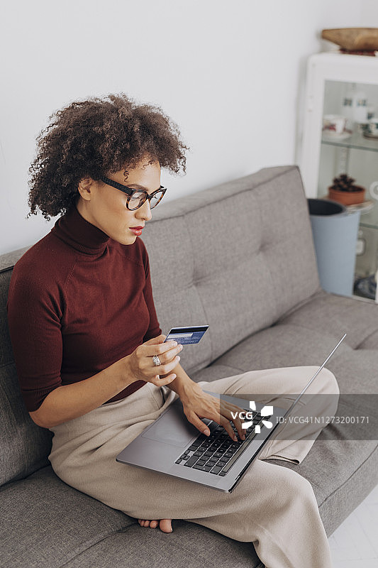网上购物:非裔美国妇女用她的信用卡在她的笔记本电脑上支付网上订单图片素材
