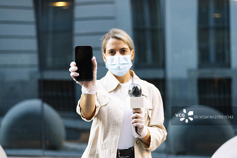 女记者戴着面具站在城市里展示智能手机图片素材