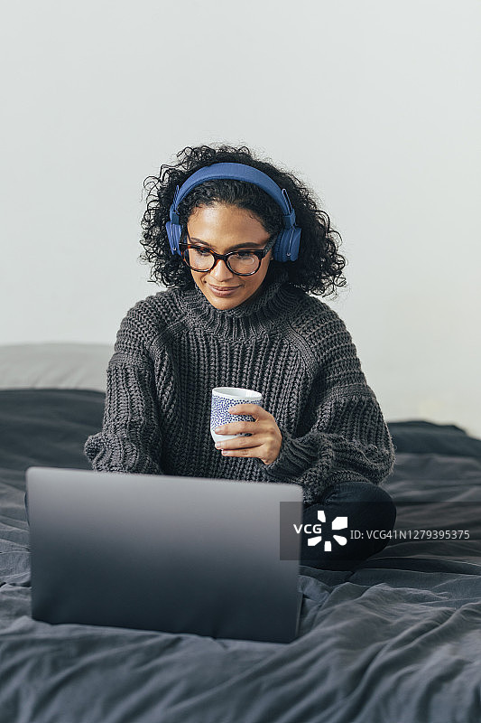 在家工作:一个年轻女人用她的笔记本电脑和一副耳机打视频电话图片素材