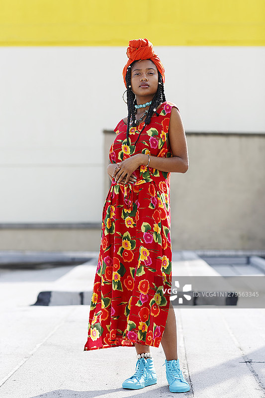 一个美丽的非裔美国妇女的肖像戴着橙色的头巾，串珠项链，花裙子，和长辫在屋顶上。图片素材