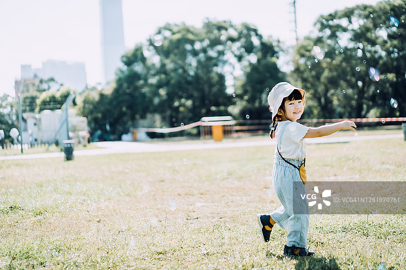 可爱的小亚洲女孩玩肥皂泡户外在一个可爱的阳光明媚的日子在自然公园的草坪上图片素材