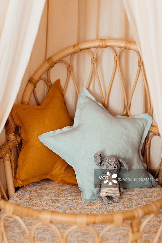 舒适的藤条婴儿床，有顶棚和枕头。高角度的星形垫子上天然亚麻布床上。有机和天然纺织品的概念。图片素材
